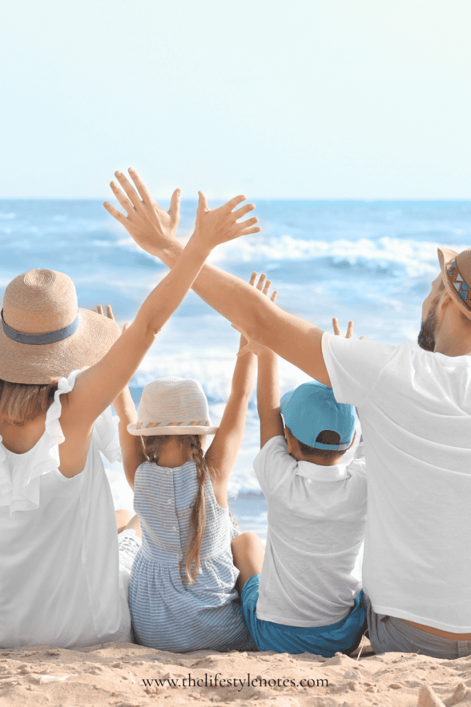 Easy Vacation Meal Planning for Families. Family of four sitting on the sand facing the ocean, with their arms in the air.