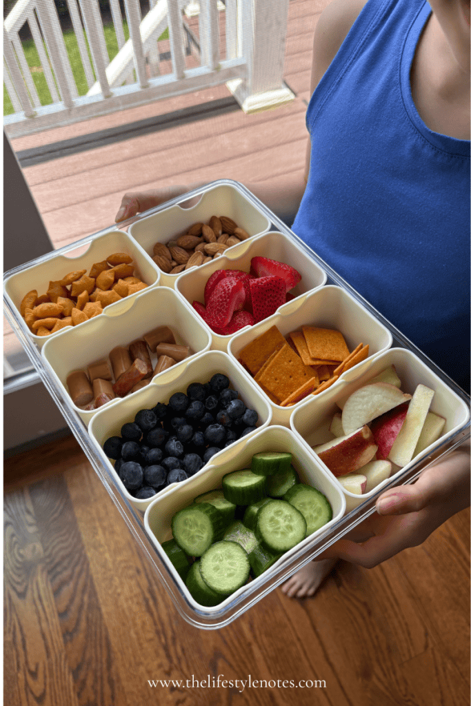 The Best Gluten Free Snack Box for Summer. Person holding a snackle box with almonds, crackers, beef stick, strawberries, blueberries, apples and cucumbers.