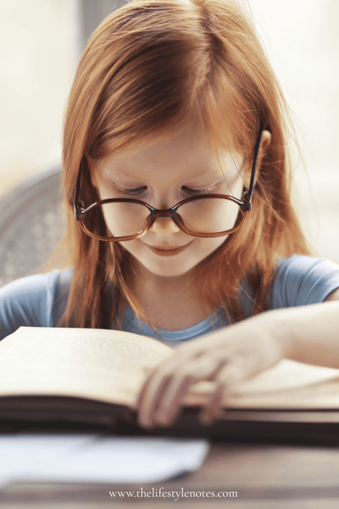 How to Create a Homework Station for Kids. Young girl with glasses sitting at a table and reading a book.