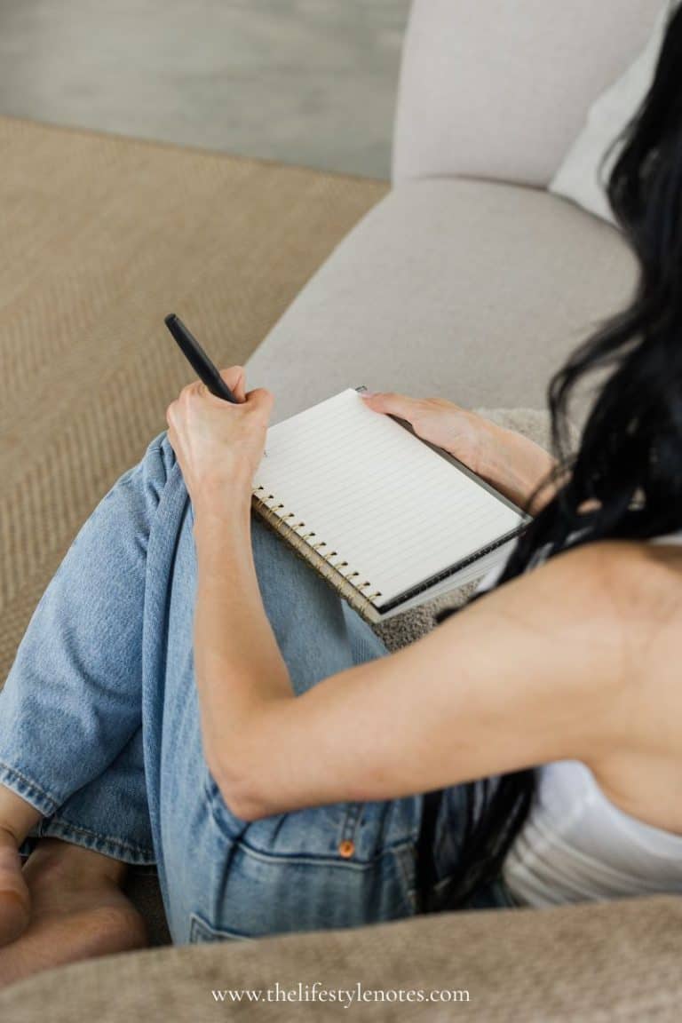 A Simple Weekly Reset Routine for Moms. Woman sitting on a couch writing in a notebook.